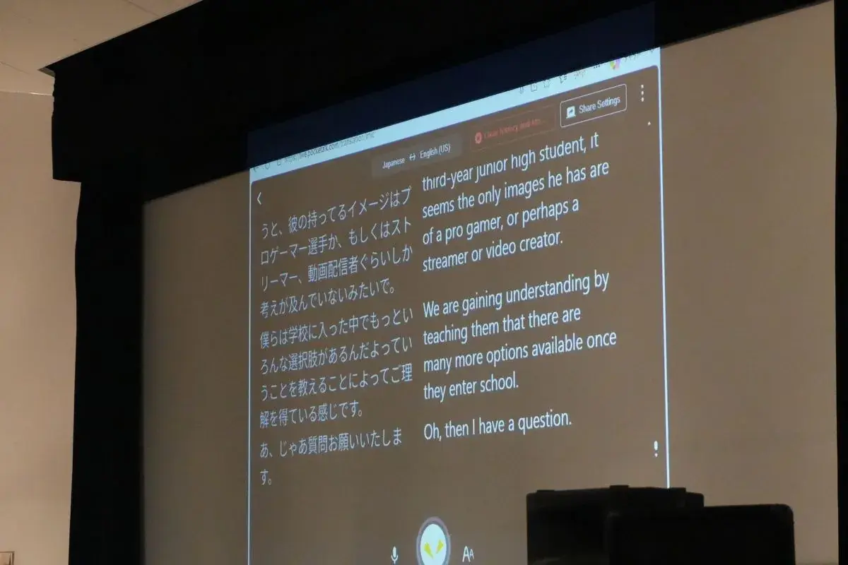 会場の大型スクリーンに、登壇者の発言が日本語と英語の対訳で表示されている