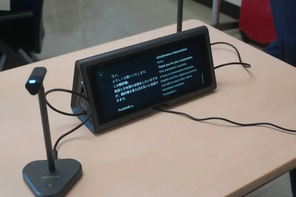 机上に置かれた据え置き型のAI通訳機「ポケトーク X」。両面ディスプレイに日本語と英語が表示されている